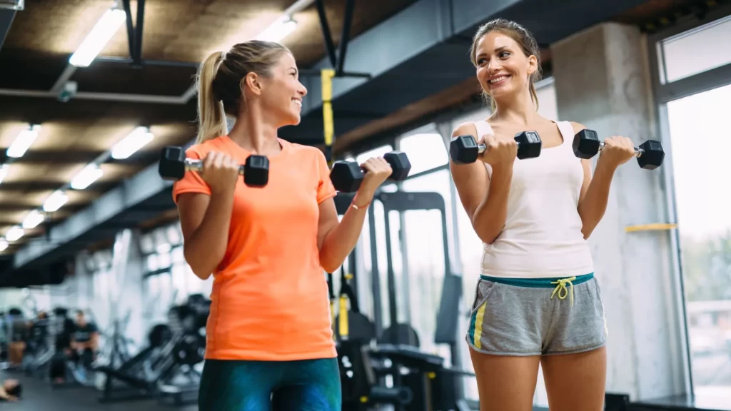Two women lifting dumbbells inside a gym 
