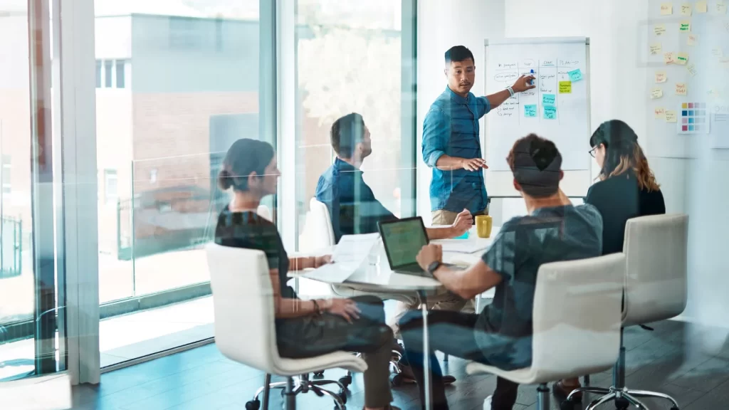 An Asian man is discussing something in front of his team inside an office conference room.