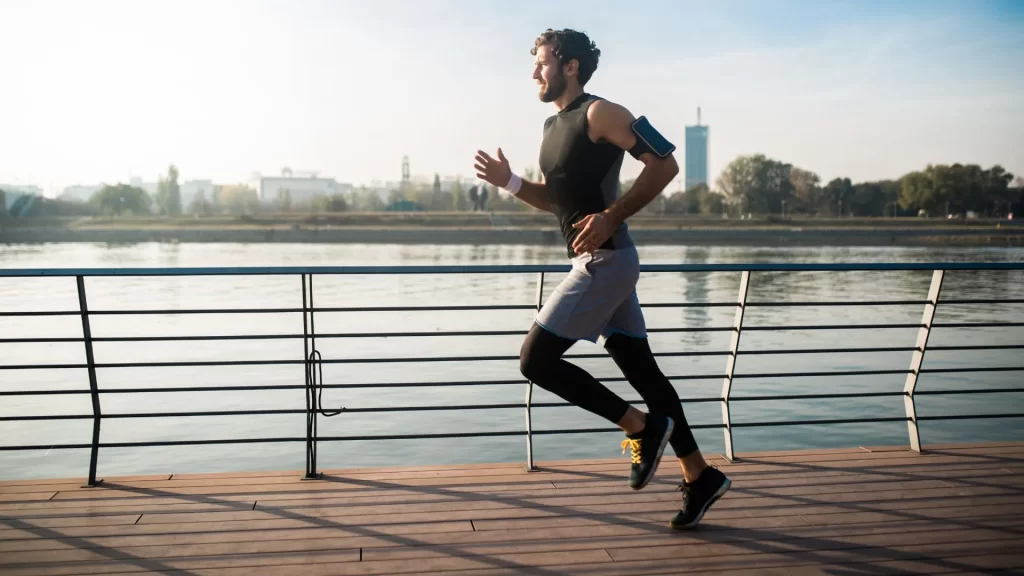 A male fitness enthusiast is jogging on the walkway beside a body of water 