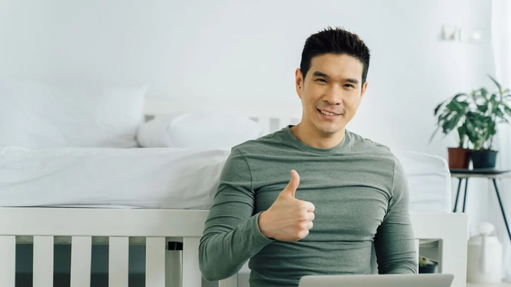 An Asian man, pictured with his laptop, doing the thumbs up sign.
