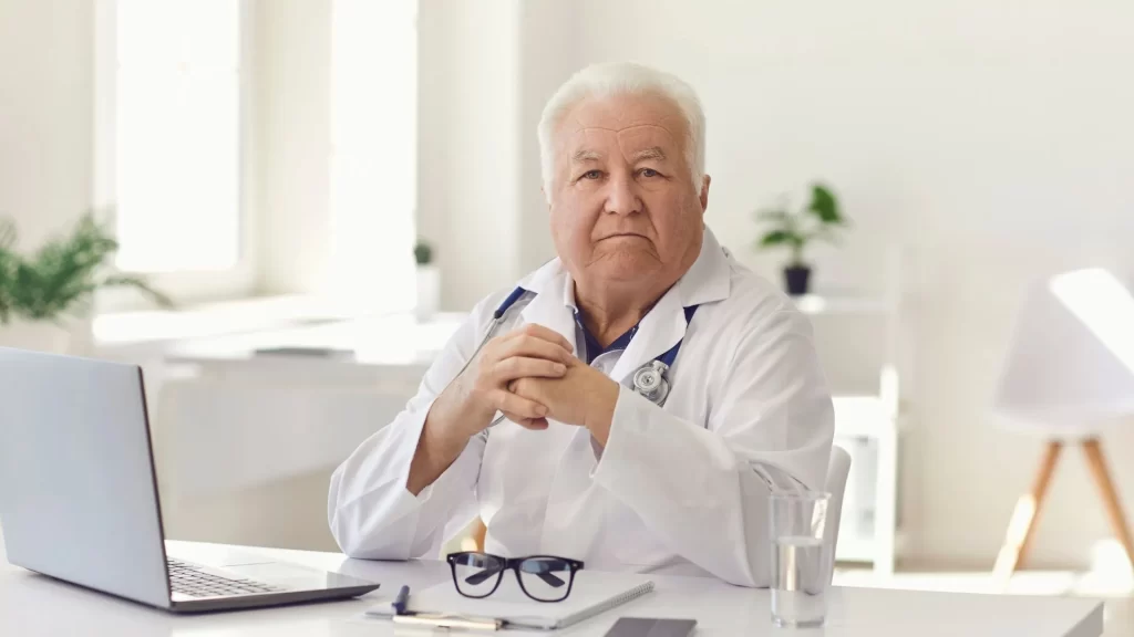 A doctor looking at the camera while his laptop is open in front of him, presumably he is studying local SEO for medical practices