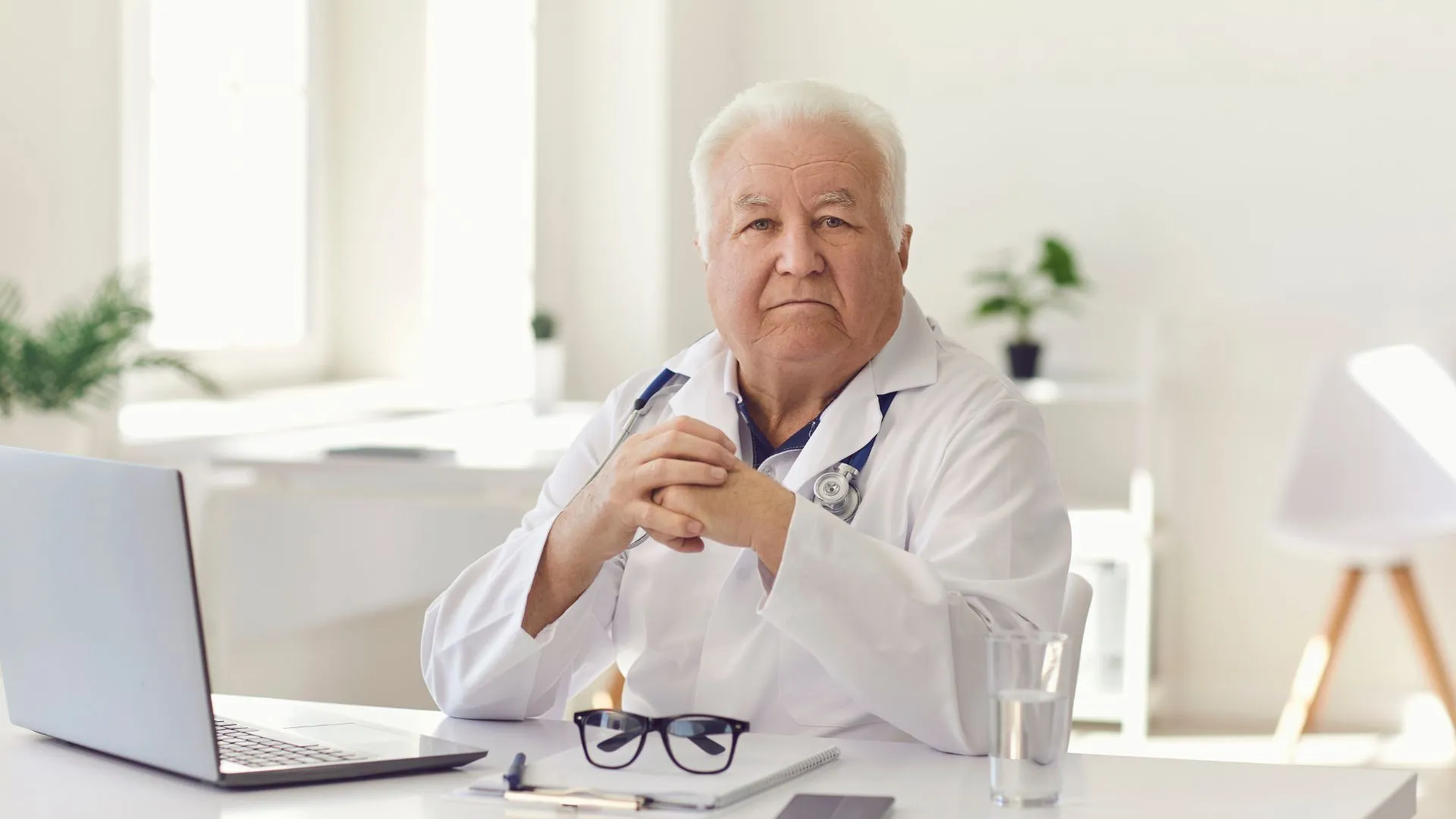 A doctor looking at the camera while his laptop is open in front of him, presumably he is studying local SEO for medical practices