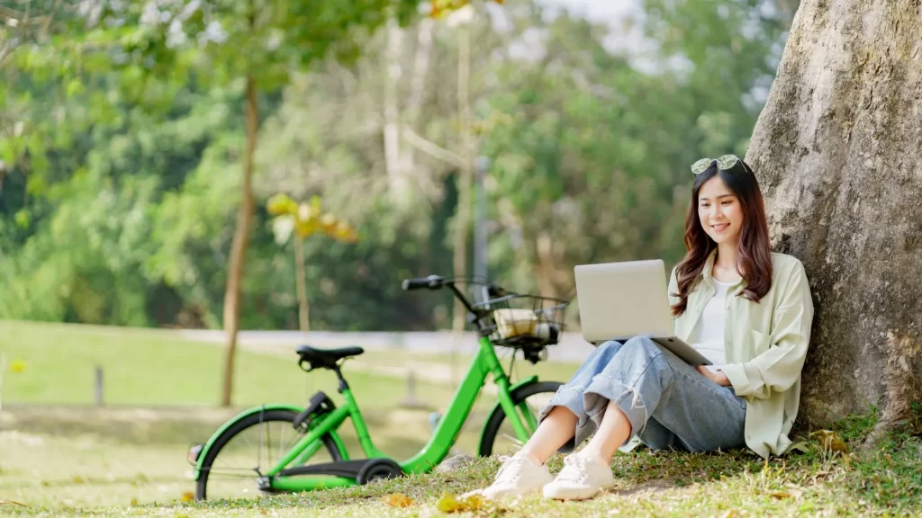 A local woman using her laptop while resting underneath the shade of a tree, presumably searching for local businesses in the area.