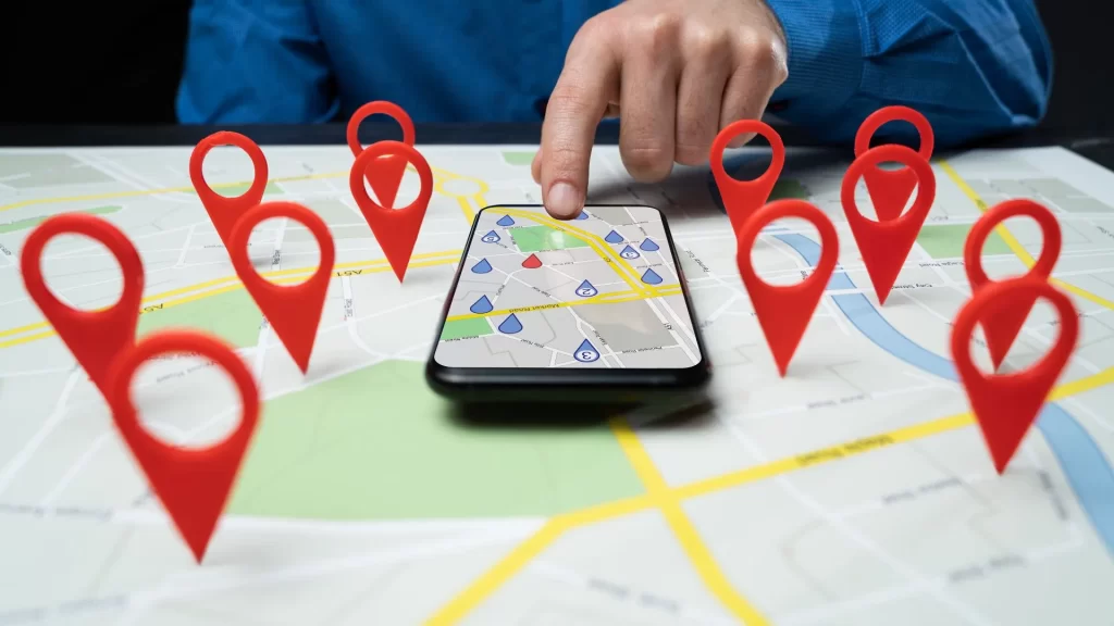 A cellphone open with Google maps. On the table where the cellphone is placed are some pins resembling Google Map icons which may symbolize local SEO